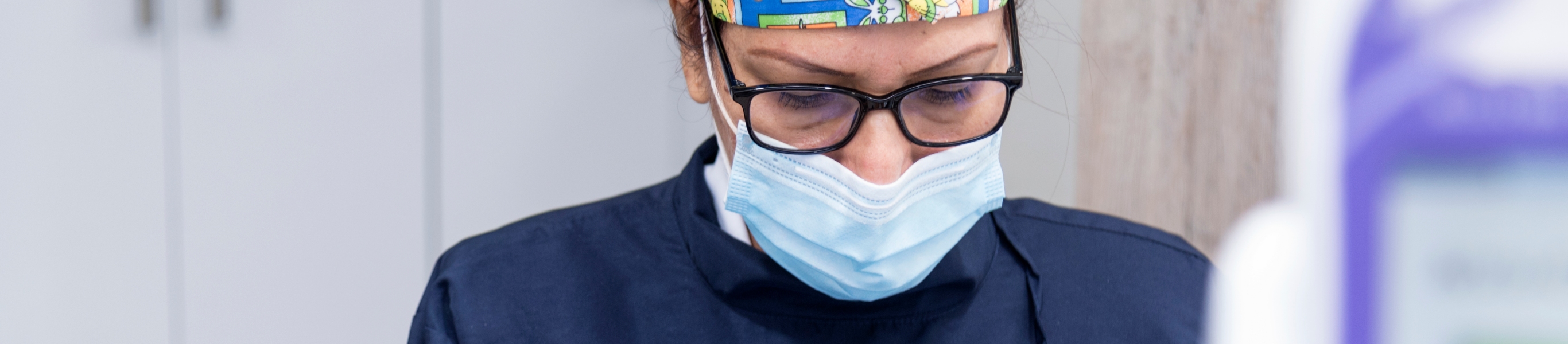 Hay una profesional de la salud que usa tapabocas, gorro quirúrgico y gafas mirando hacía abajo. 